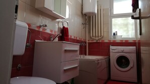 Een kleine badkamer met toilet, wastafel, spiegel en een wasmachine.