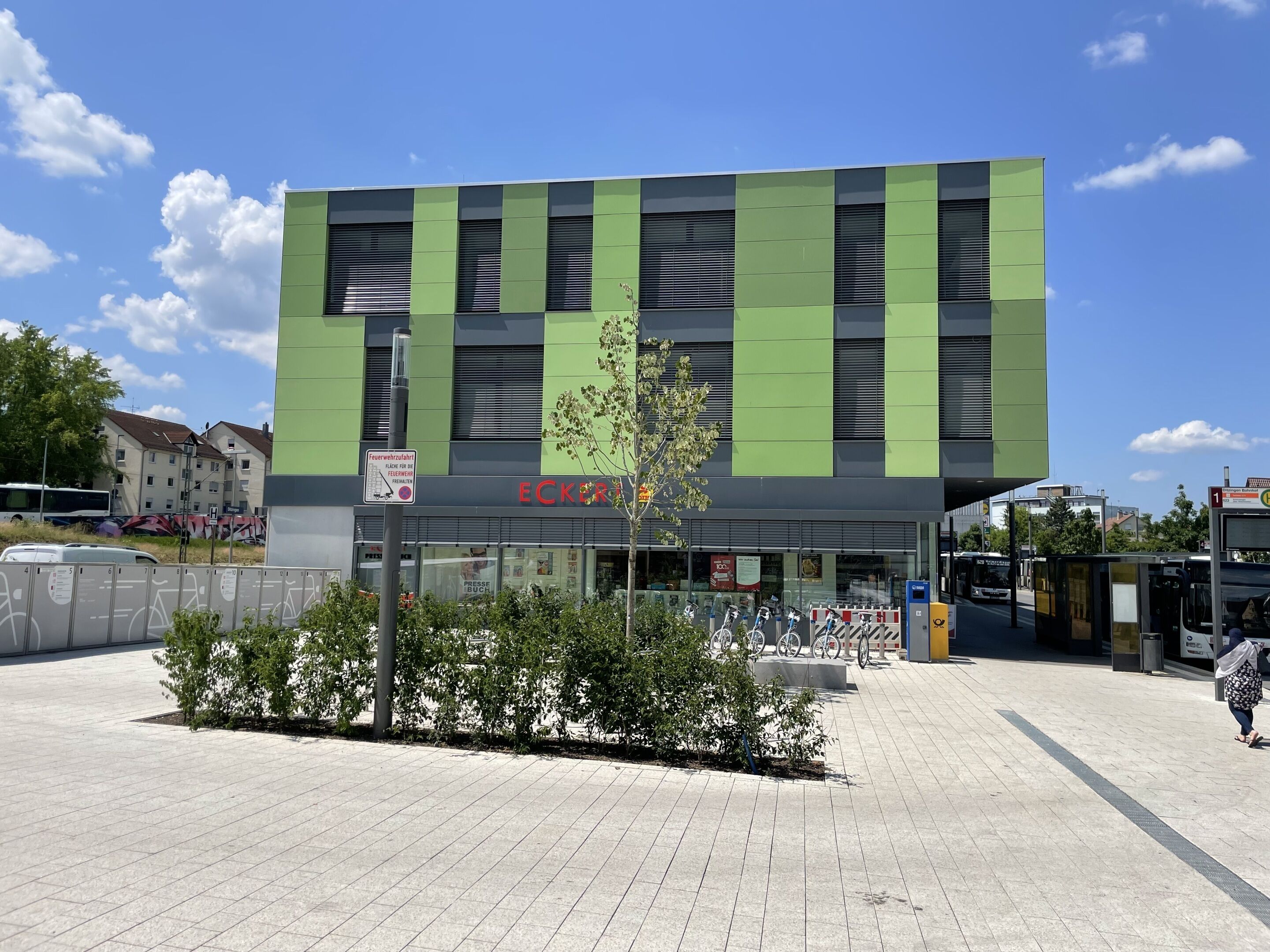 A modern building with a green and black facade, a visible entrance, and a parking area with bicycles.