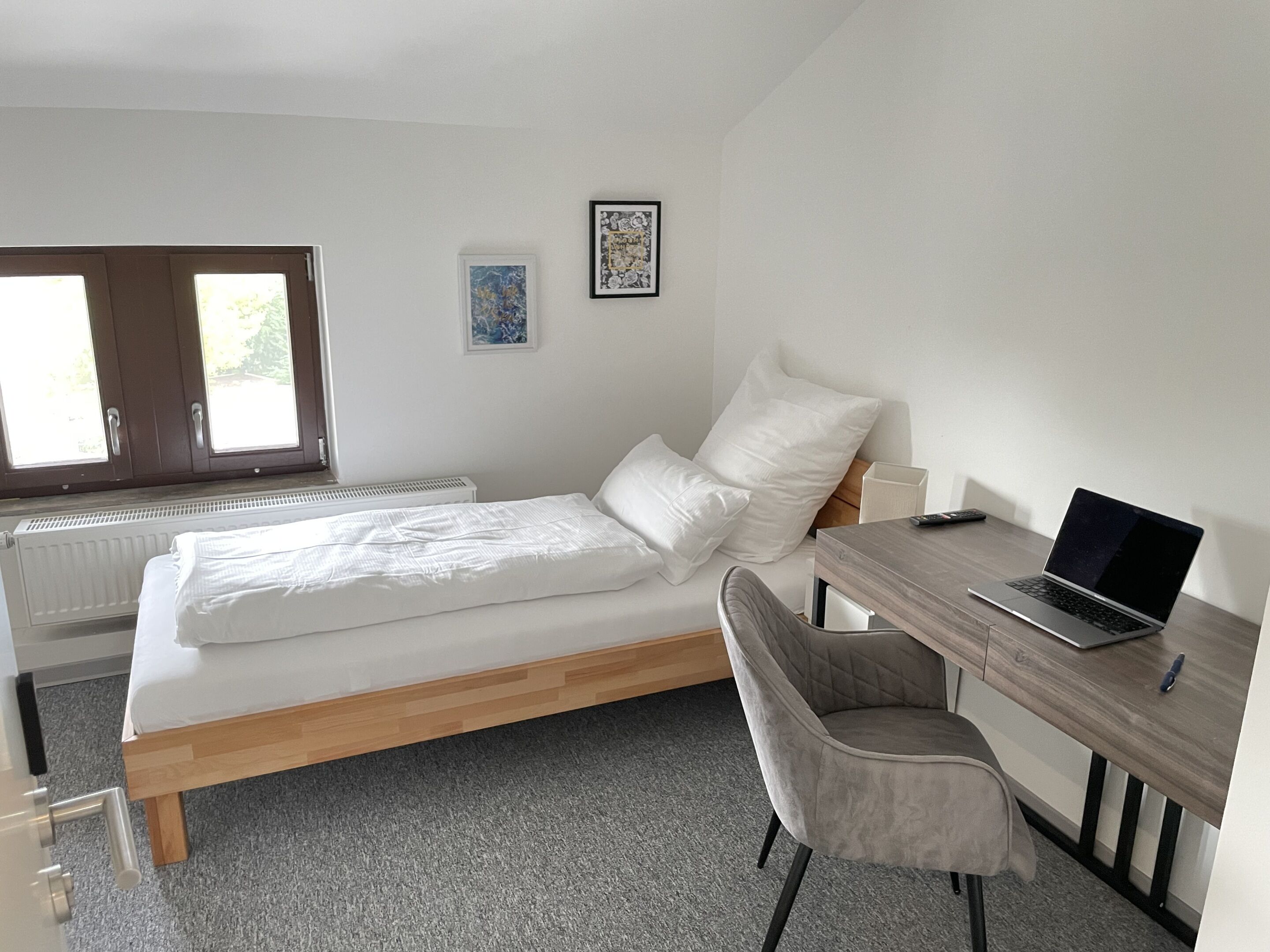 A bedroom with a bed, a desk, a chair, a radiator, and two windows.