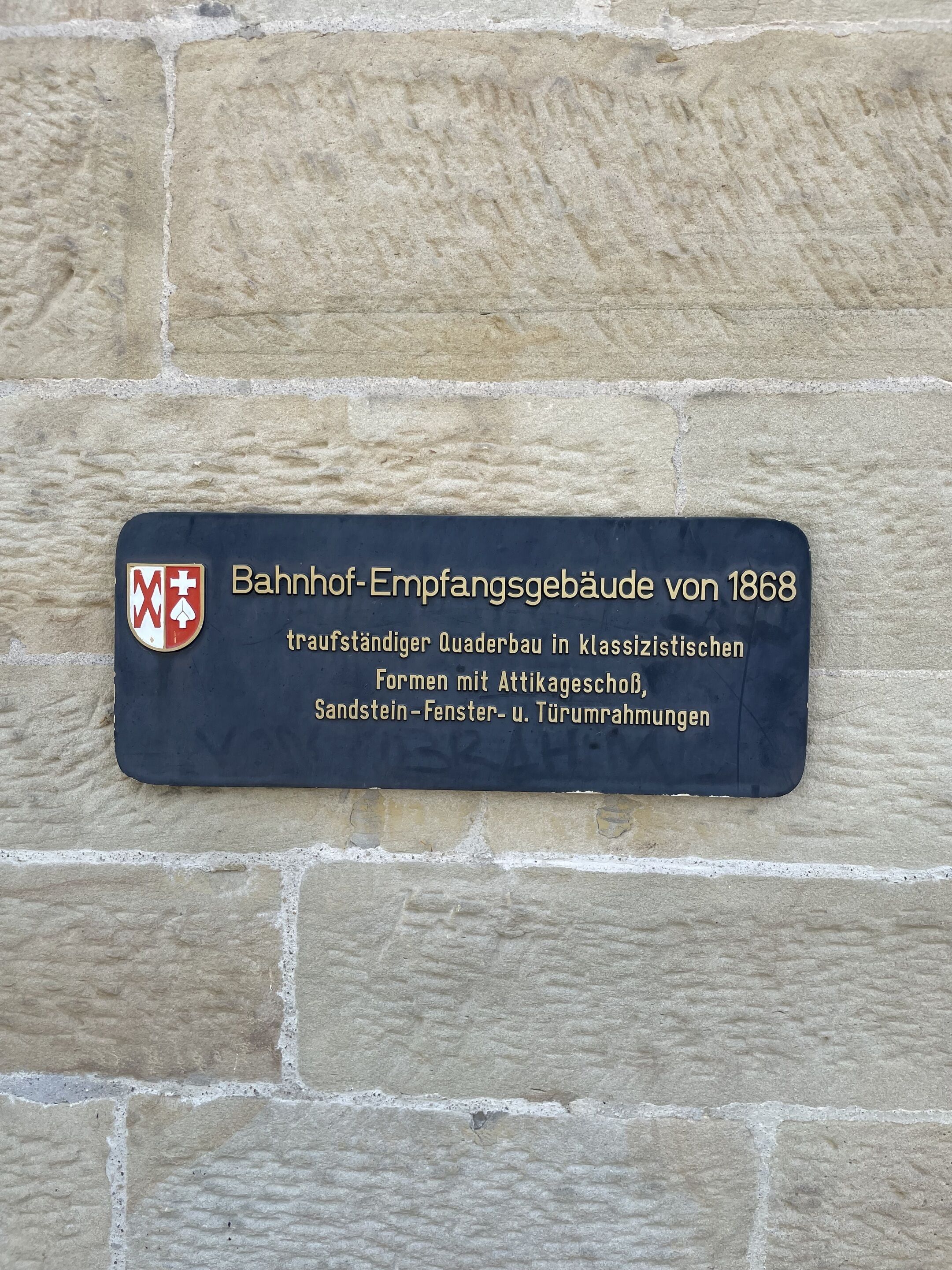 Ein historisches Gebäudeschild mit Wappen und Text, der ein traditionelles Nebengebäude aus dem Jahr 1868 beschreibt.