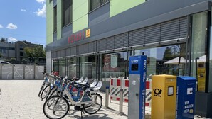 A building with a sign reading "ECKERT" and a lottery advertisement. There are bicycles parked in front, and a blue and yellow box with text. - Hotel am Bahnhof Ditzingen (Ditzingen)