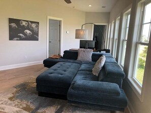 A living room with a sectional sofa, a rug, a painting, a door, and a window.