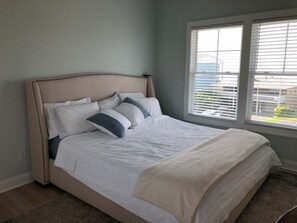 A bedroom with a bed, a window with blinds, and a view of a building outside.