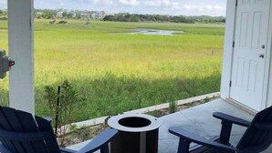 Un porche cubierto con dos sillas Adirondack, una mesita redonda y vistas a un campo verde y una masa de agua.