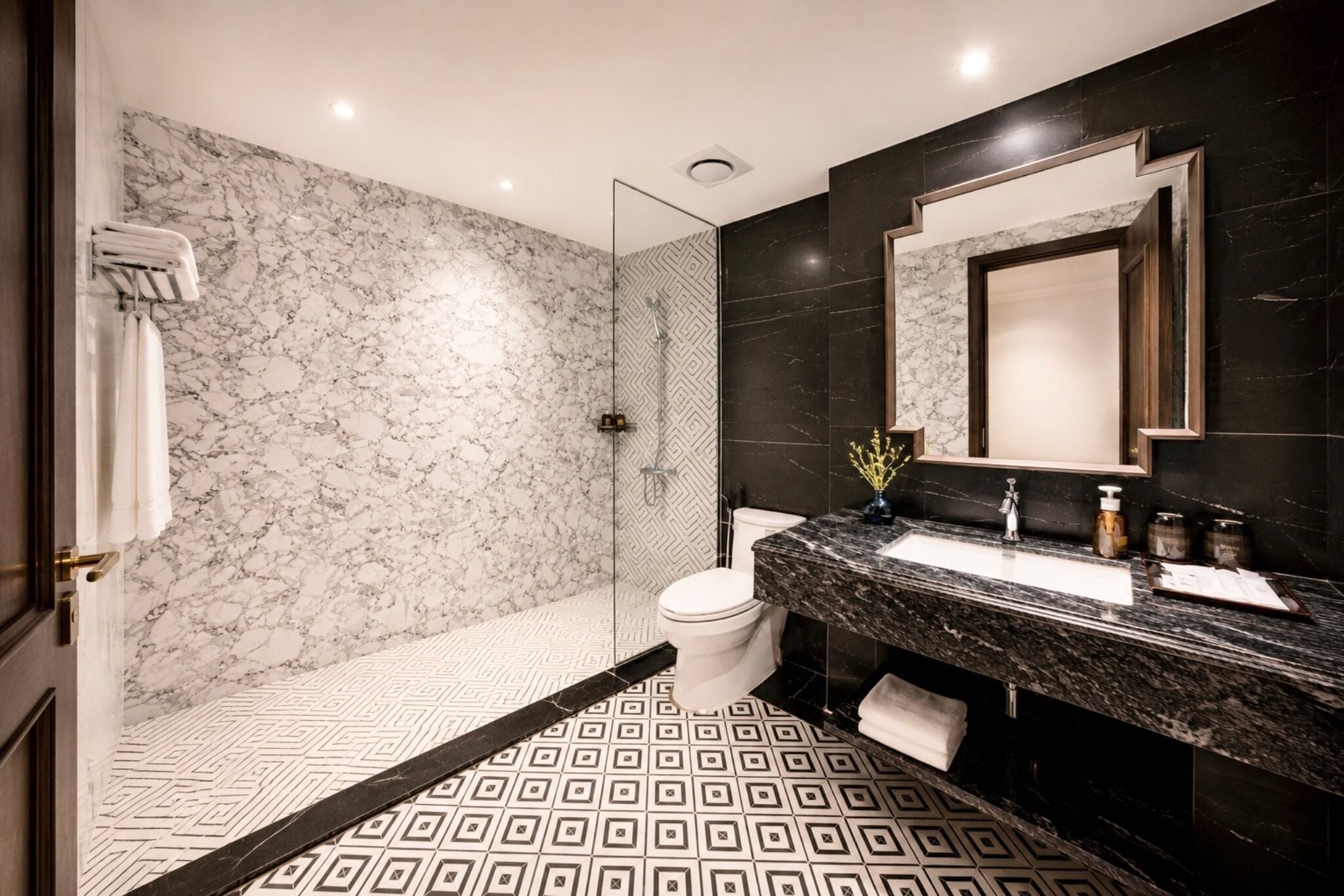 Un baño moderno con pared de mármol, ducha con cerramiento de vidrio, lavabo de mármol negro y suelo estampado.