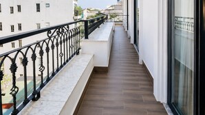Ein Balkon mit Marmorboden, schwarzem Geländer und Blick auf angrenzende Gebäude.
