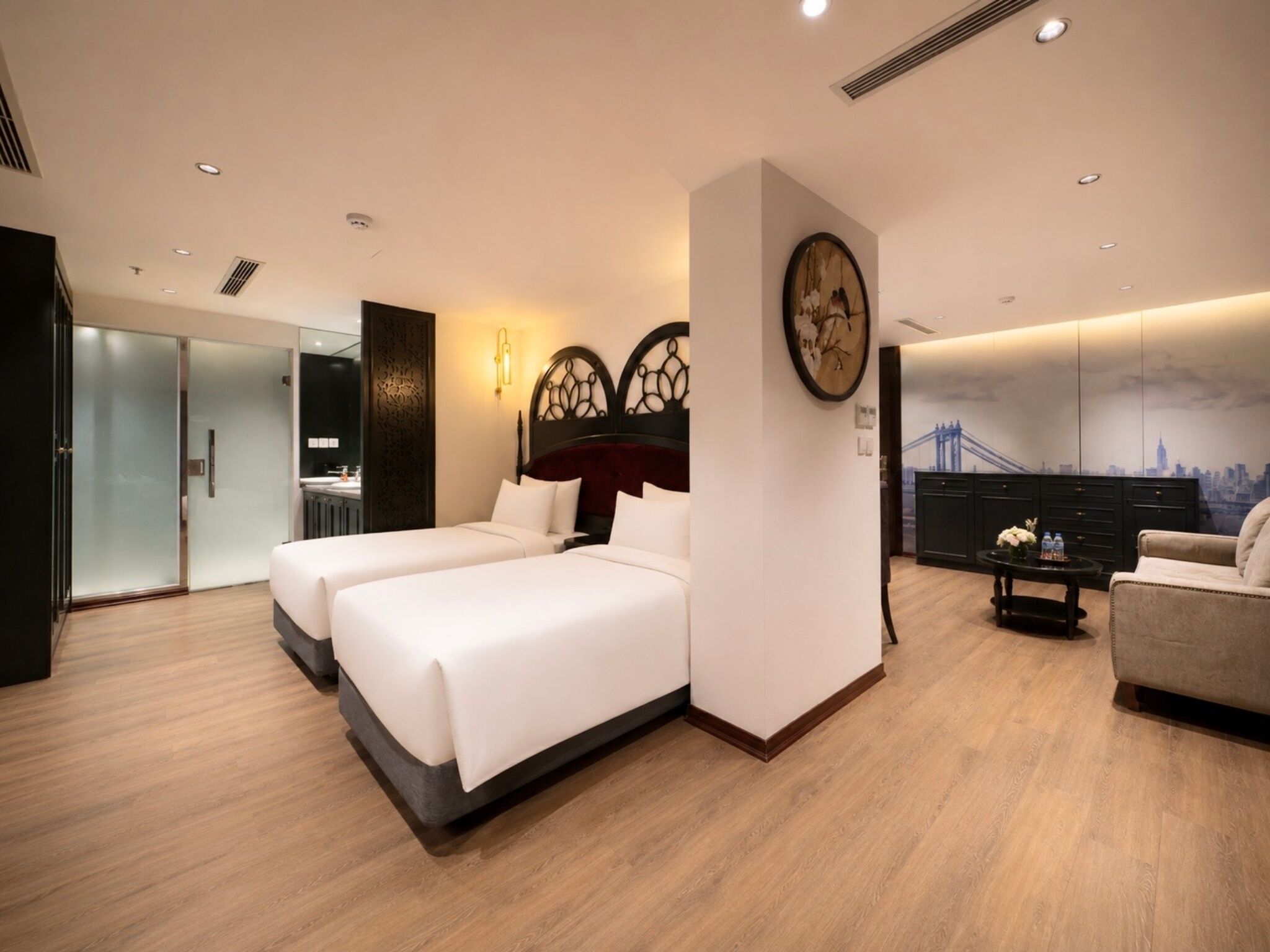 Habitación de hotel con dos camas, un escritorio, una silla y un mural con vista a la ciudad.