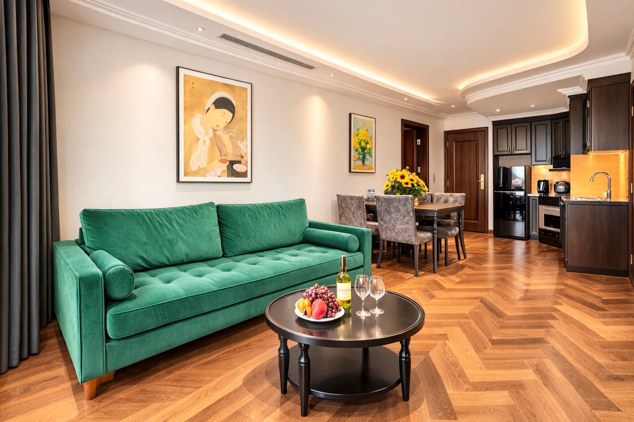 A modern living room with a green sofa, a dining table with chairs, a kitchen area, and artwork on the walls.