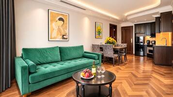 A modern living room with a green sofa, a dining table with chairs, a kitchen area, and artwork on the walls.