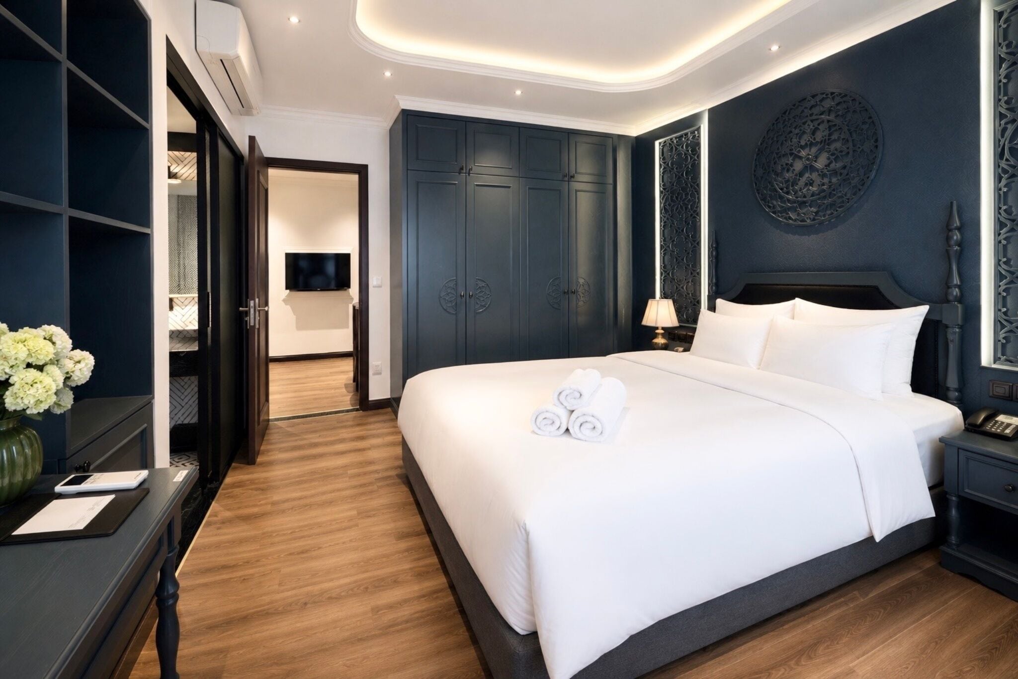 Ein Hotelzimmer mit einem großen Bett, einem dunkelblauen Kleiderschrank, einem Flachbildfernseher und einem Wandbild.