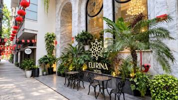 Ein Hotel Eingang mit einer Schrifttafel mit der Aufschrift 'ELIRINA HOTEL', Außenbestuhlung und roten Laternen.