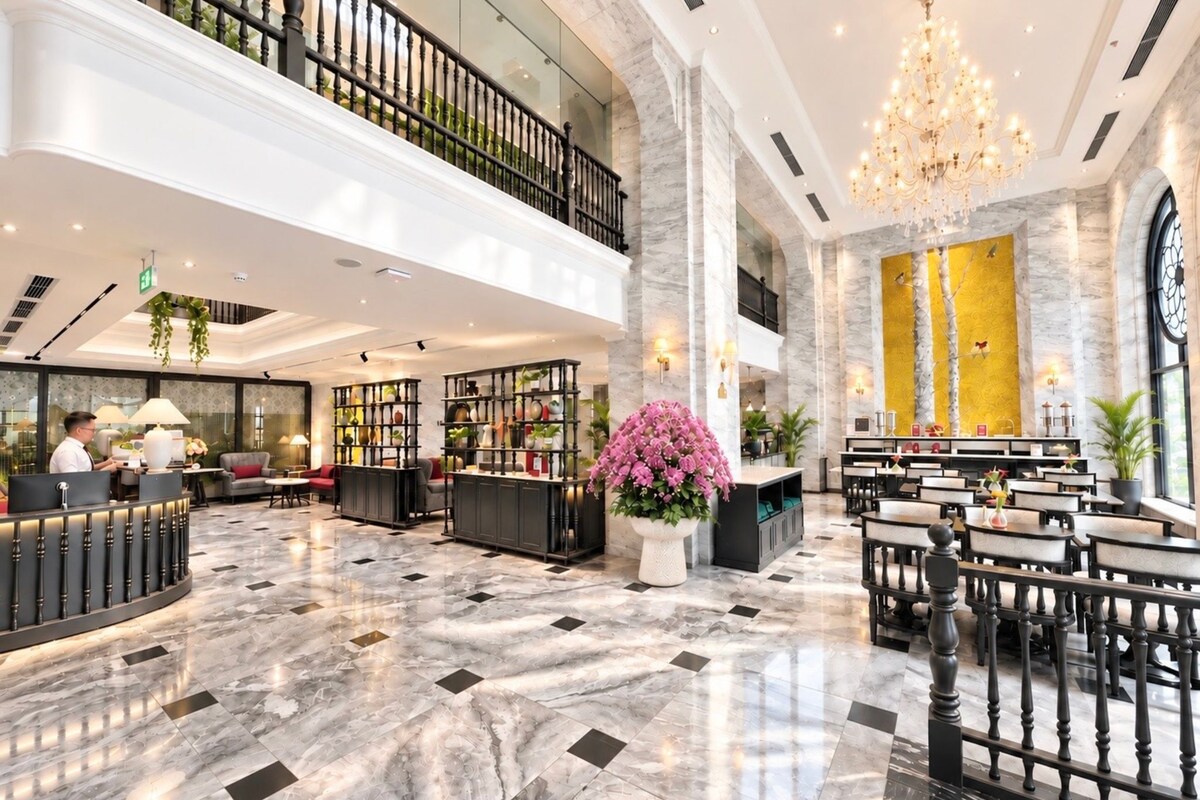 A hotel lobby with a reception desk, seating area, and a chandelier.