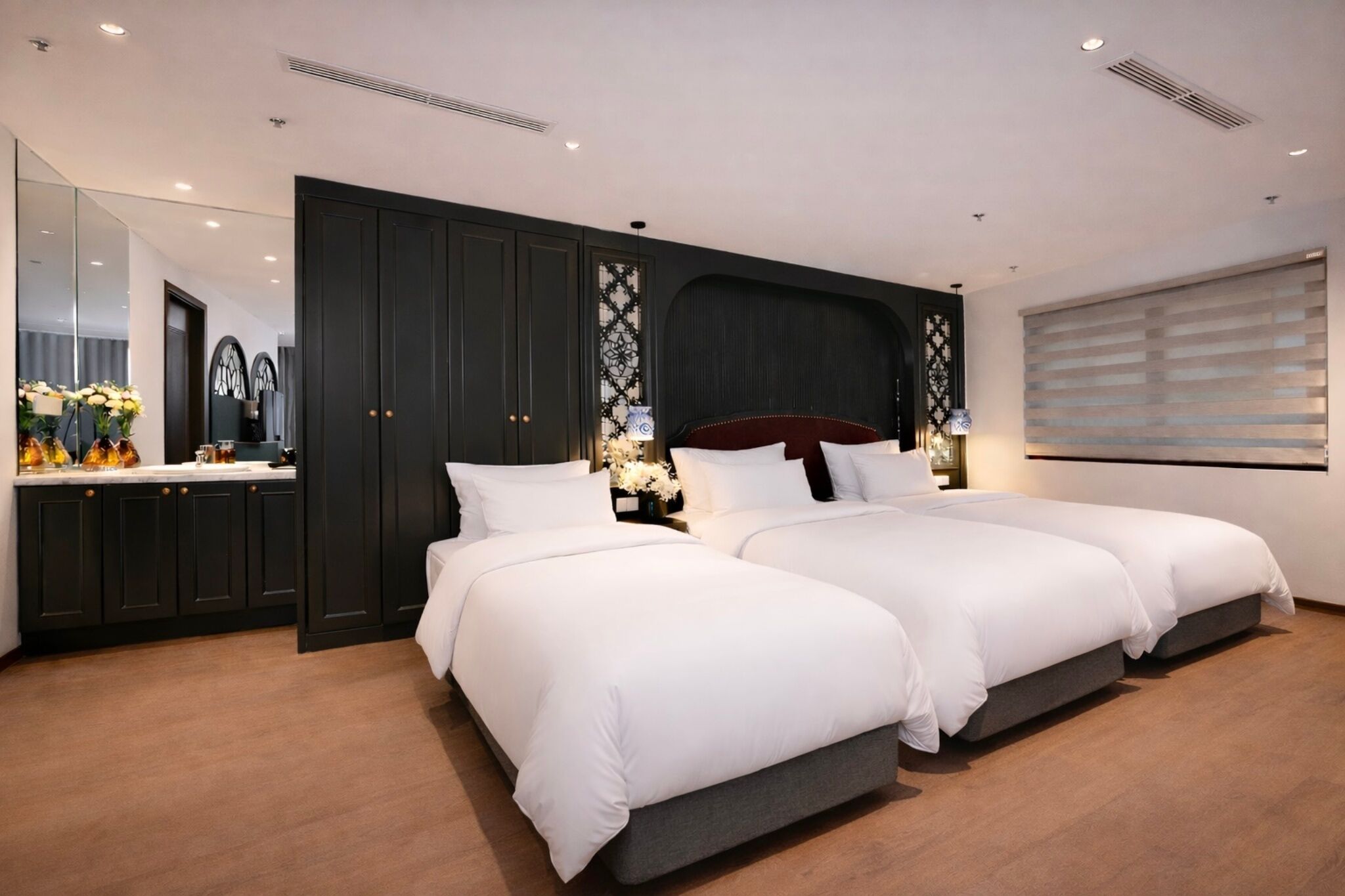 Een moderne slaapkamer met twee bedden, donkerhouten kasten, een grote spiegel en een raam met jaloezieën.