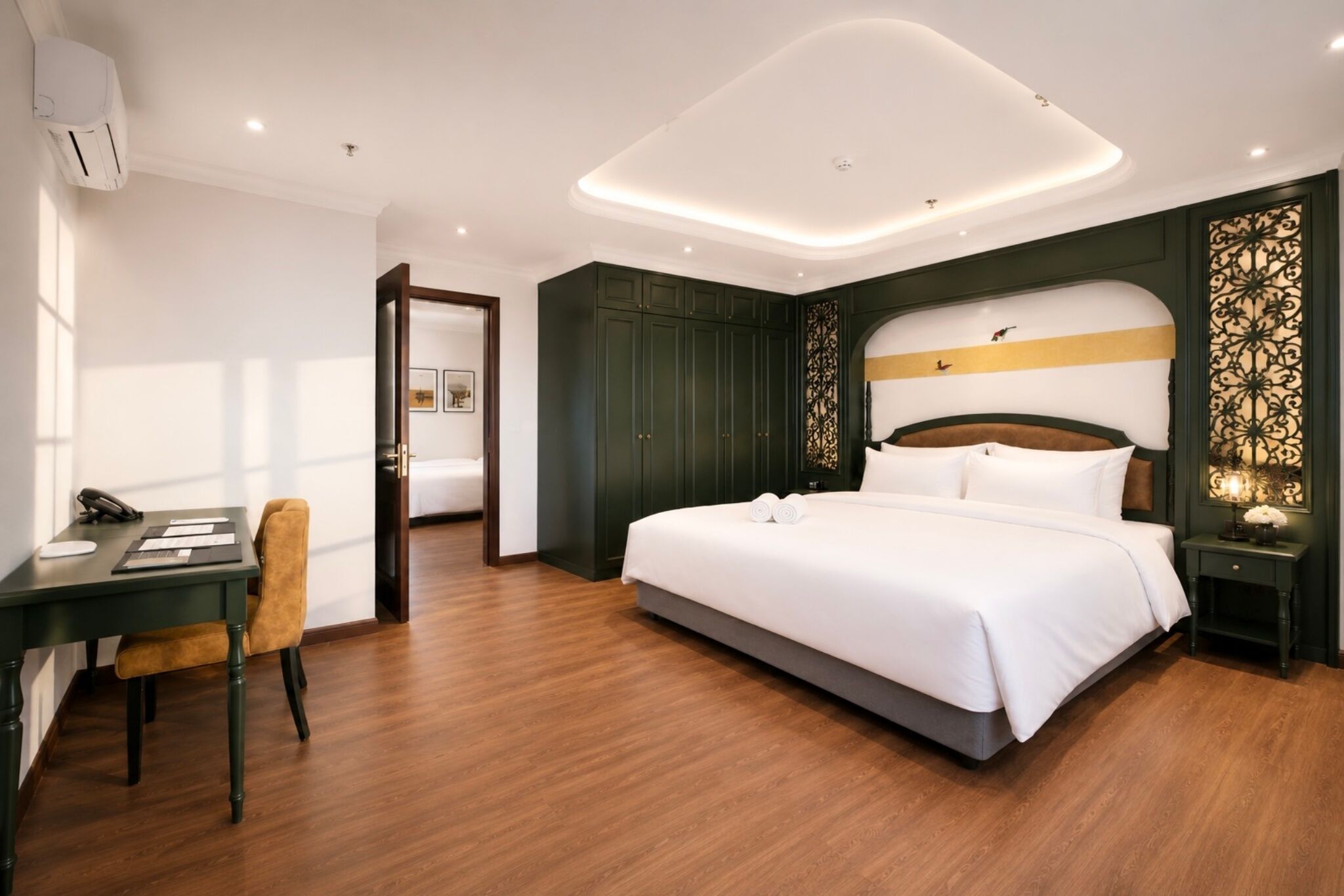A modern hotel room with a large bed, a desk with a chair, and a wardrobe.