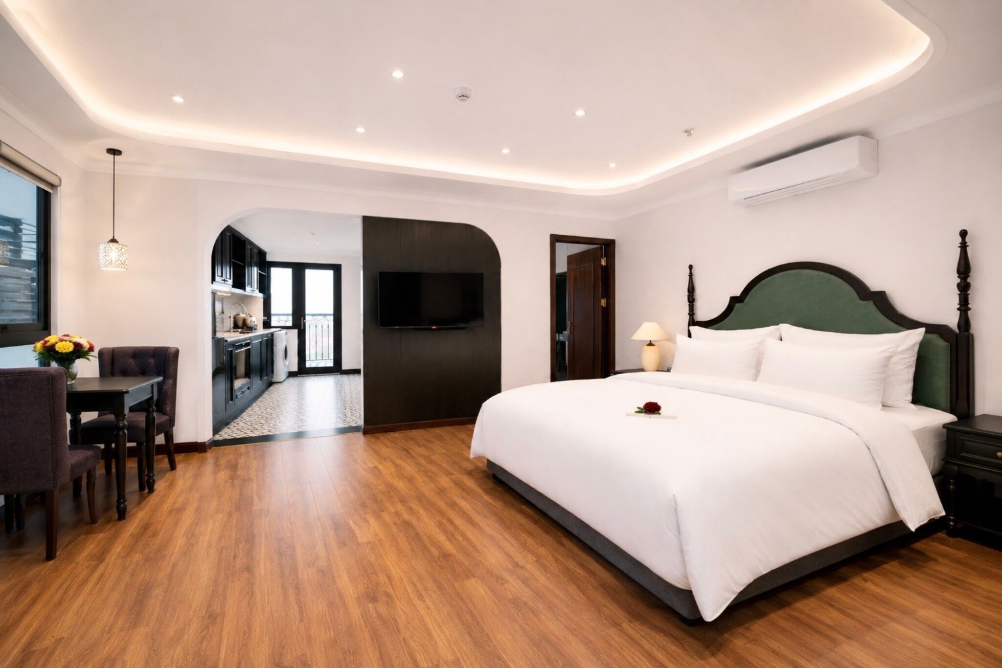 A hotel room with a large bed, a TV, a dining area, and a view of the city.