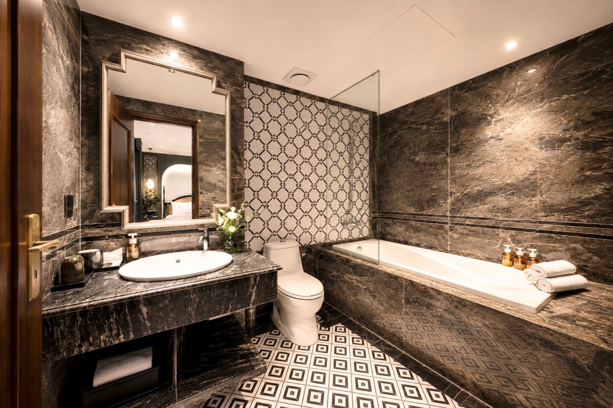 Un baño moderno con lavamanos, inodoro y bañera de mármol, con piso de diseño geométrico y paredes de mármol oscuro.