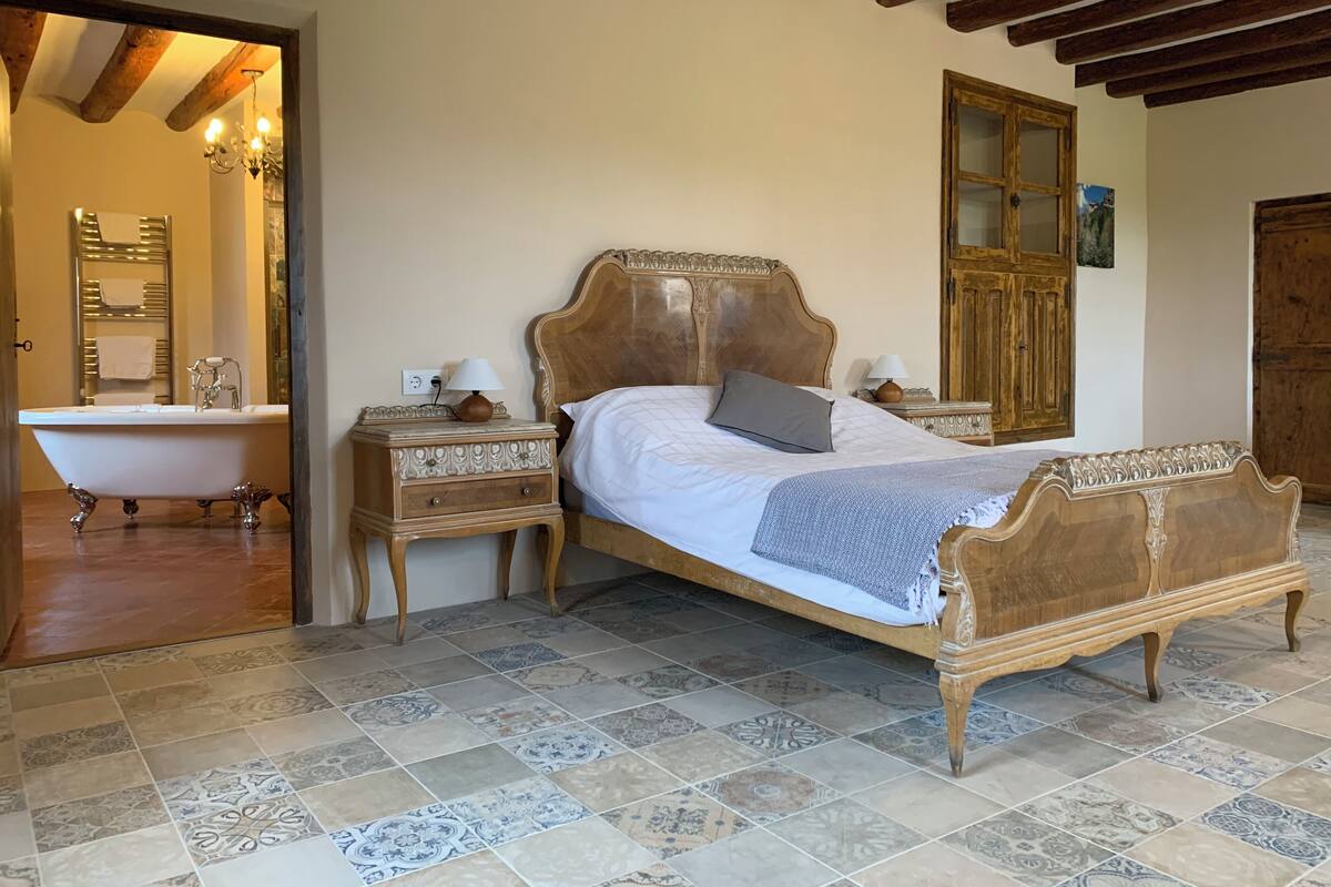 A bedroom with a large bed, a wooden nightstand, a classic lamp, and a vintage-style bathtub.