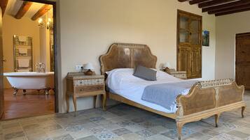 A bedroom with a large bed, a wooden nightstand, a classic lamp, and a vintage-style bathtub.