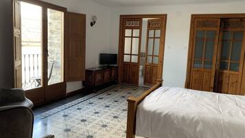 A bedroom with a bed, a television on a wooden cabinet, and a balcony door leading to an outdoor area.