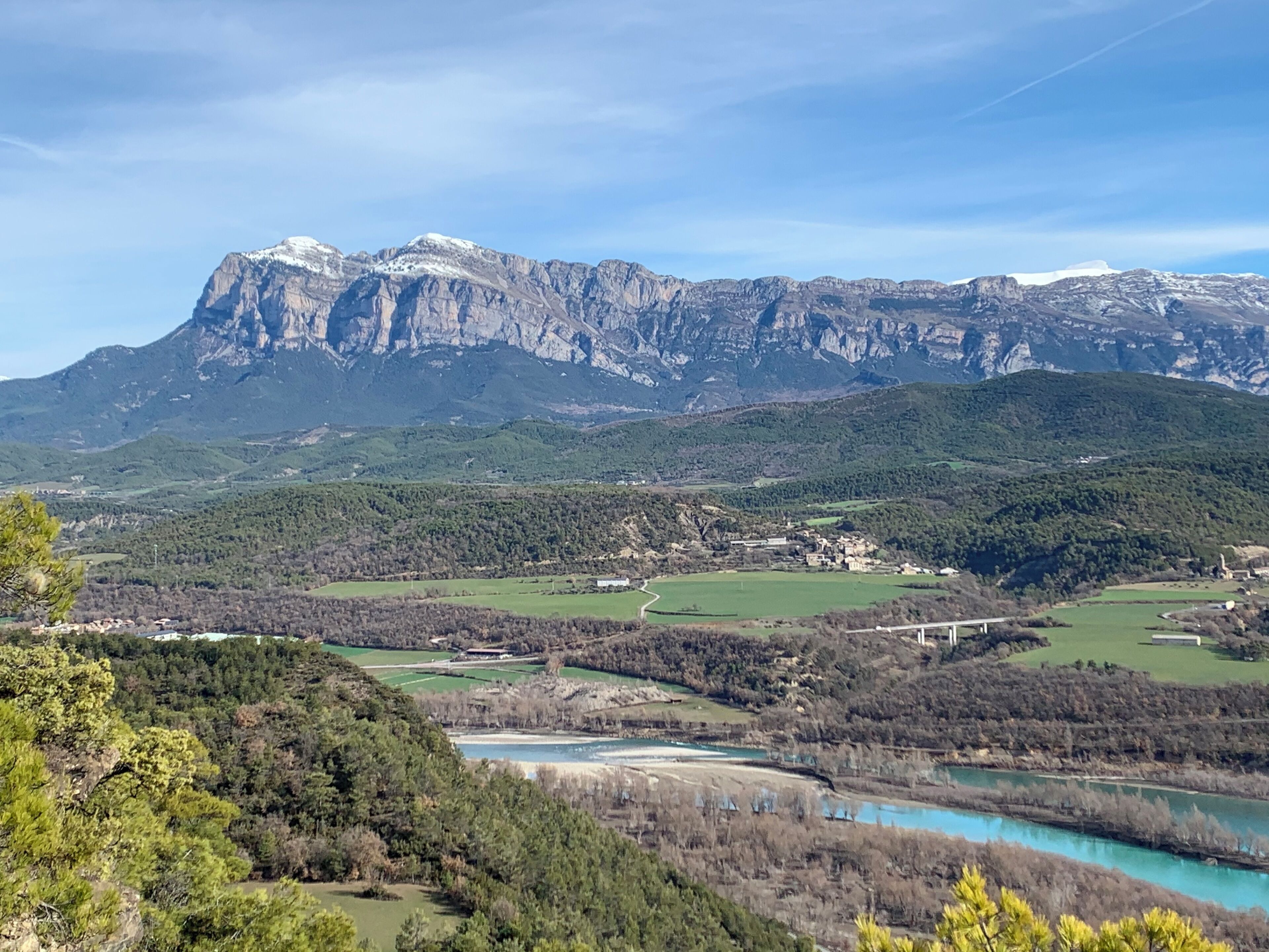 A mountainous landscape with a river, green fields, and a bridge.
