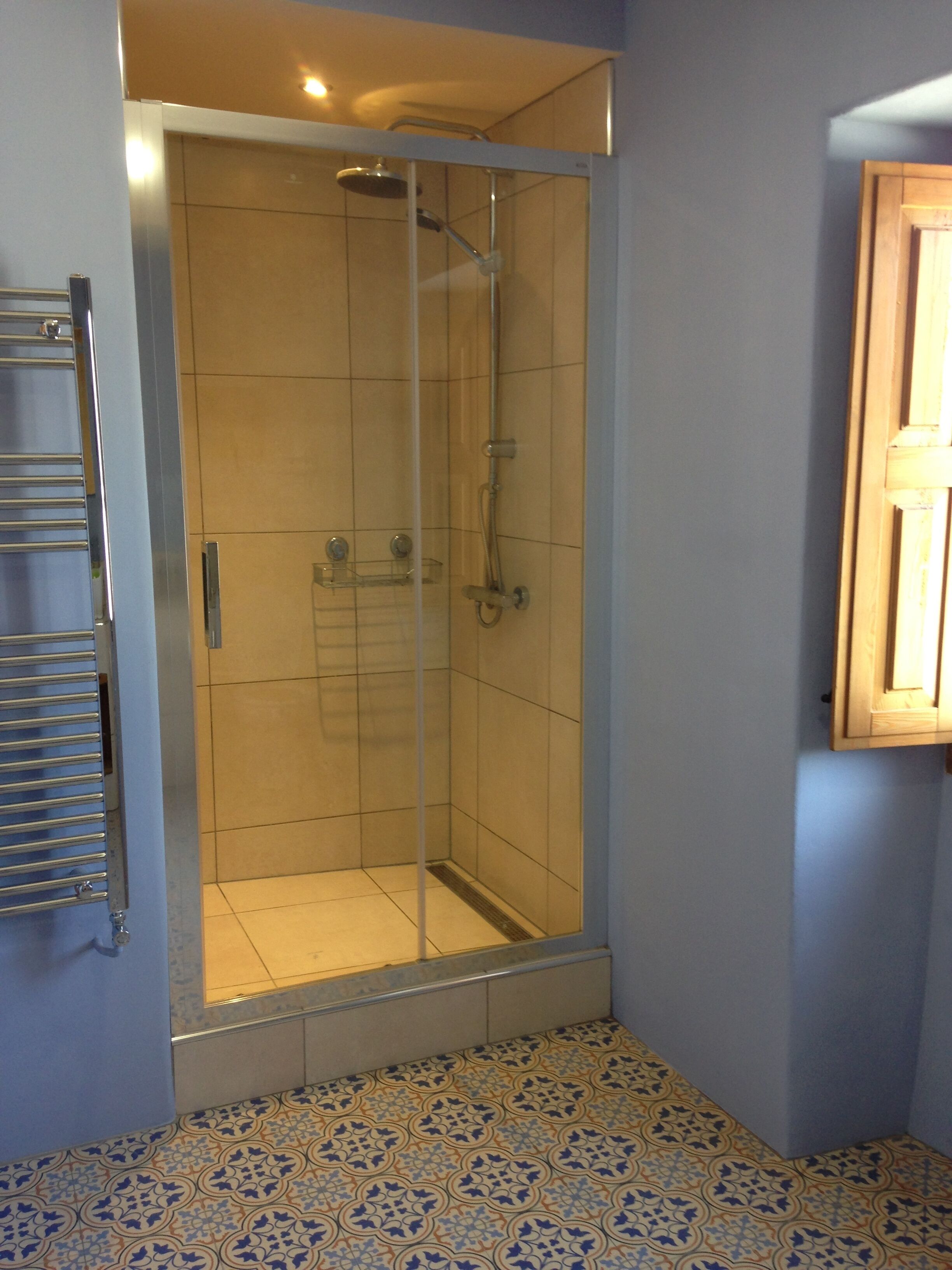 Une salle de bain avec une douche à parois de verre, un sol carrelé et un porte-serviettes.