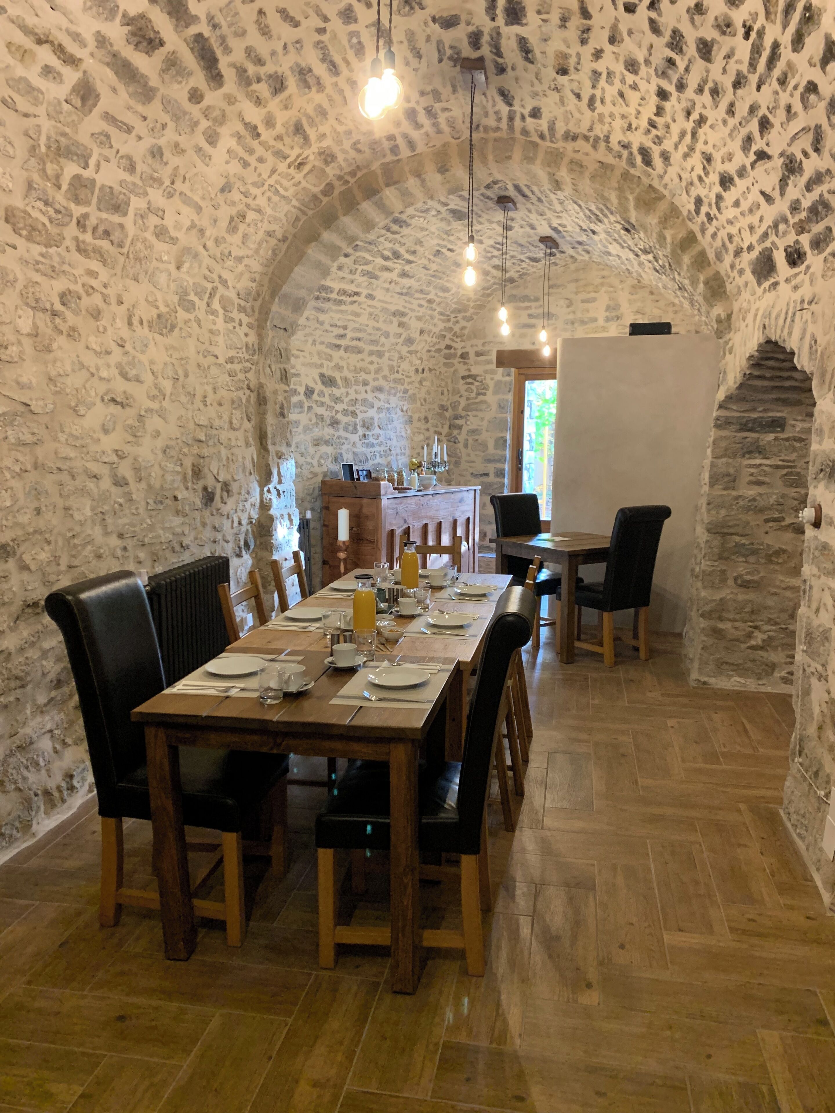 Comedor con paredes de piedra, una larga mesa de madera dispuesta para cuatro personas, sillas negras y una pizarra en la pared.