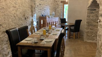 Comedor con paredes de piedra, una larga mesa de madera dispuesta para cuatro personas, sillas negras y una pizarra en la pared.