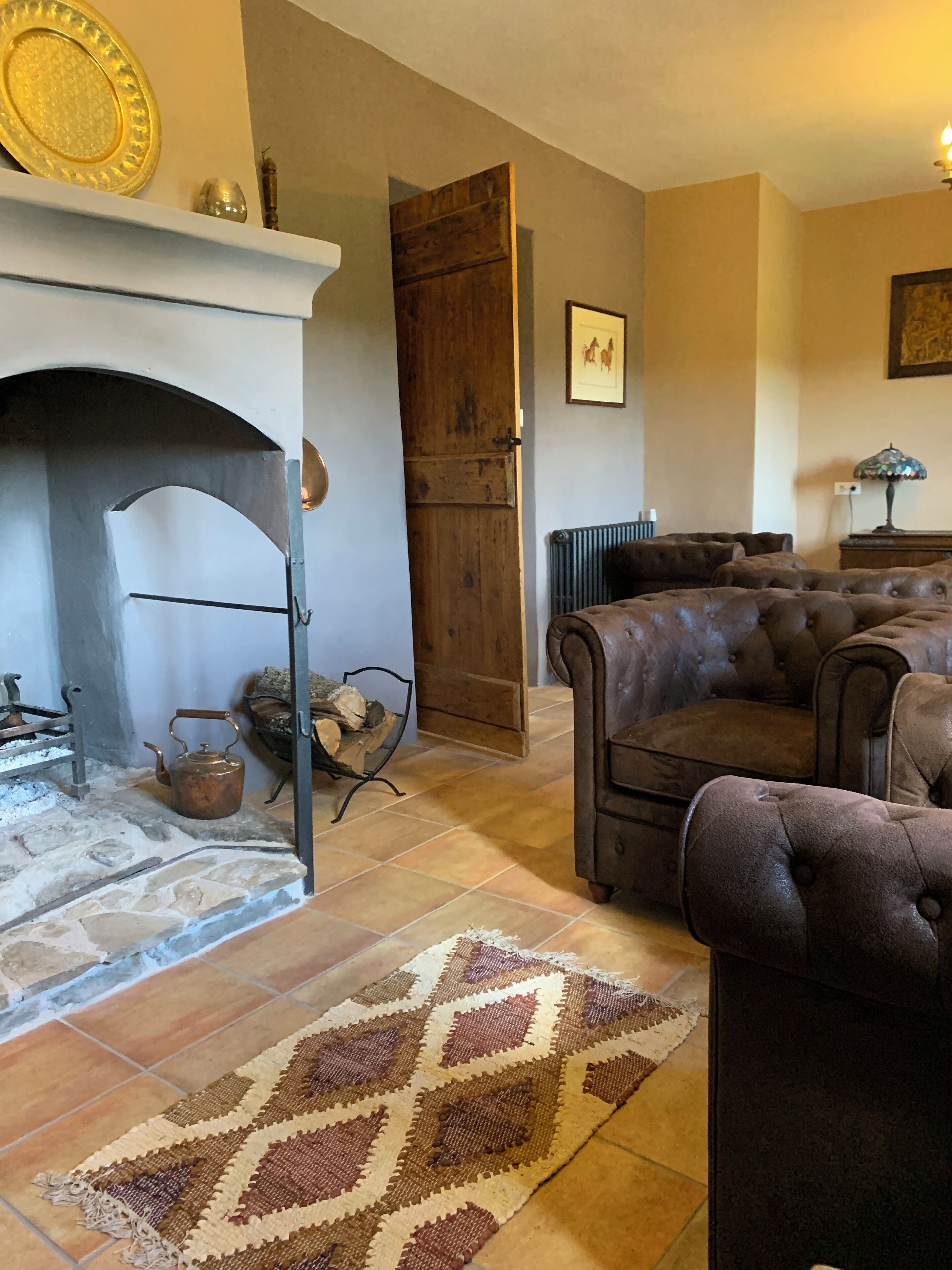 Una sala de estar acogedora con chimenea, un sillón grande, un tapete estampado y una puerta de madera.