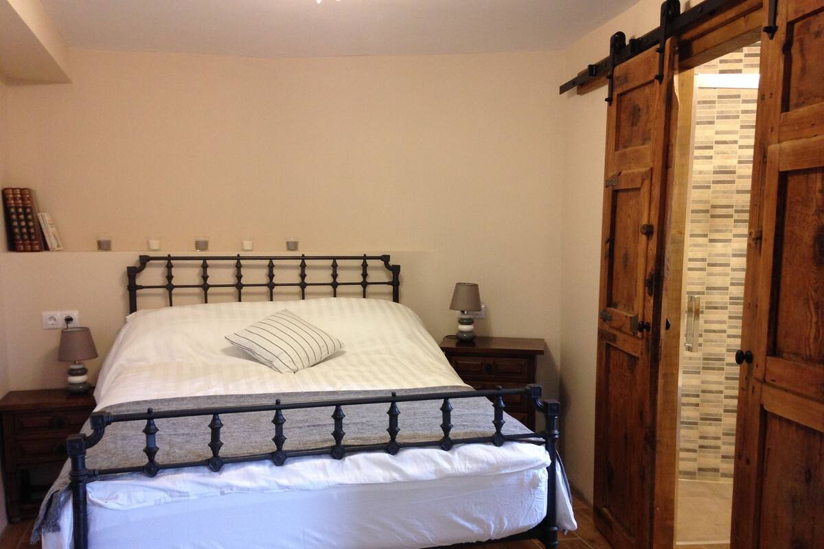 A bedroom with a bed, wooden wardrobe, and a nightstand with a lamp.
