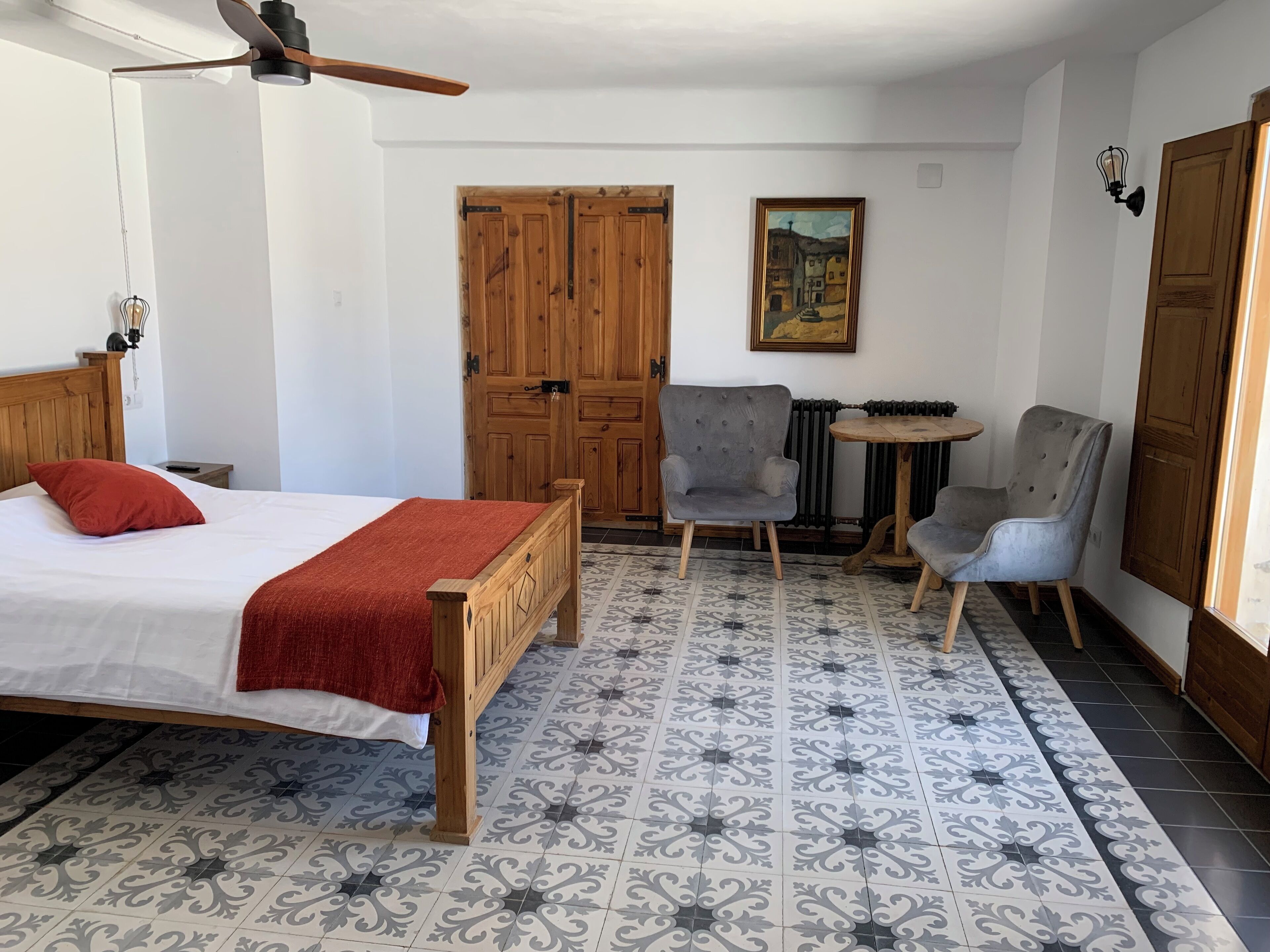 A bedroom with a wooden bed, a red throw, a grey armchair, a small round table, and a radiator.
