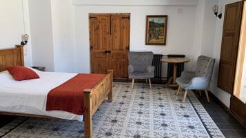 A bedroom with a wooden bed, a red throw, a grey armchair, a small round table, and a radiator.
