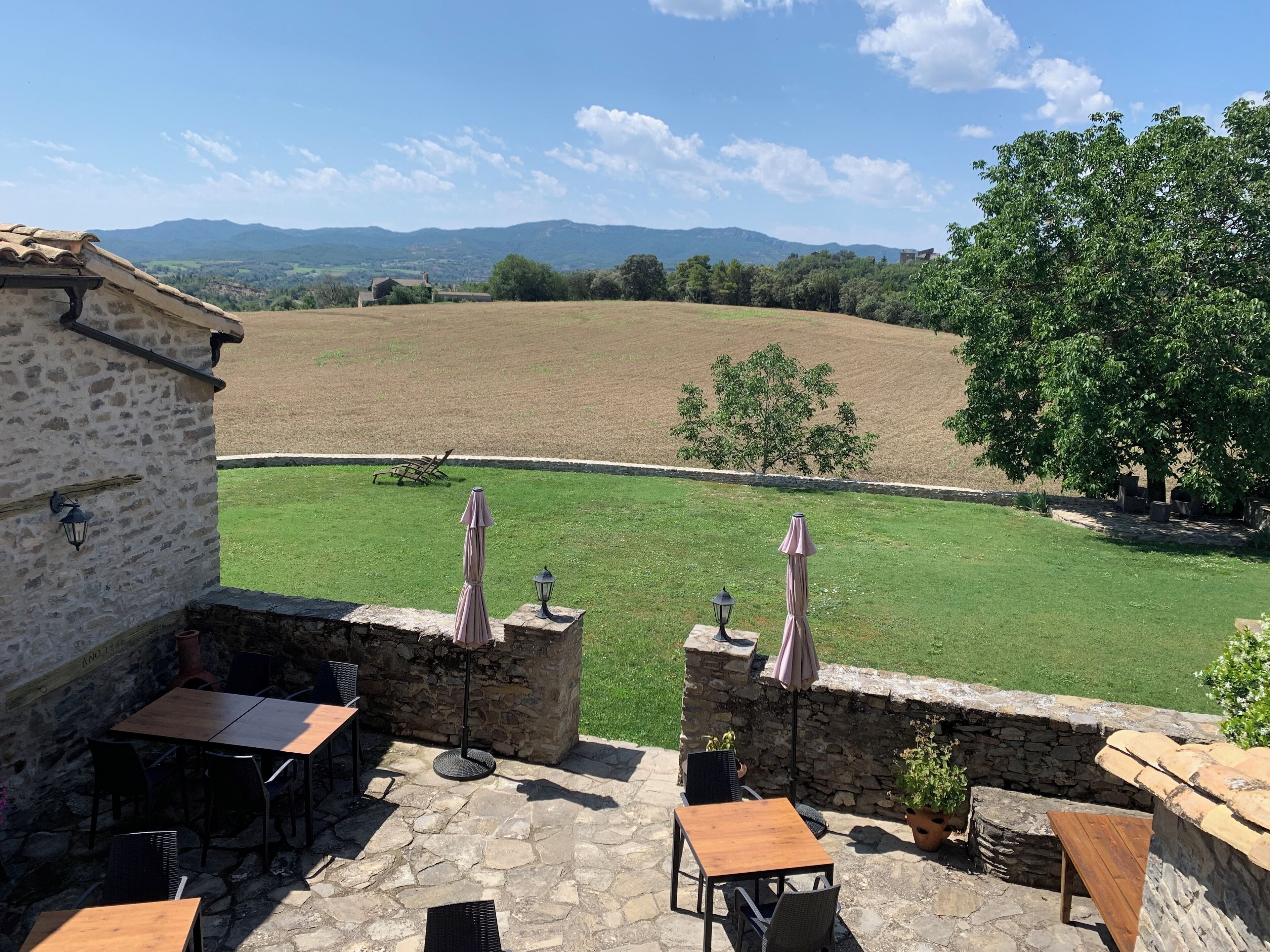 A stone patio with outdoor seating, a view of a green field, and a stone building.