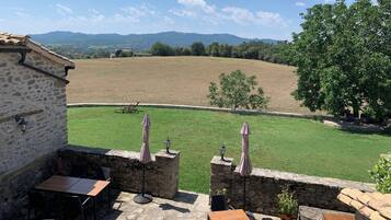 A stone patio with outdoor seating, a view of a green field, and a stone building.