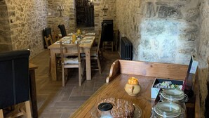 A rustic stone-walled dining area with a wooden table set for a meal, including fruits, a cake, and a milk jug. - Casa Lascorz (Ainsa)