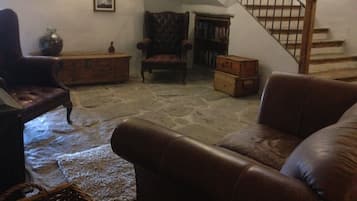 Una sala de estar acogedora con suelo de piedra, sofás de cuero, un cofre de madera y una escalera.