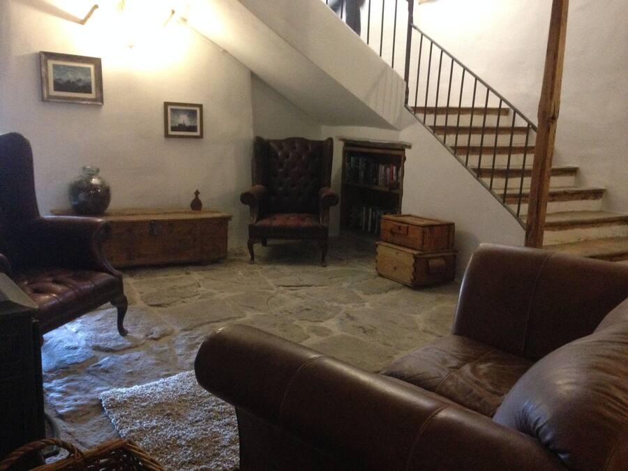 Una sala de estar acogedora con suelo de piedra, sofás de cuero, un cofre de madera y una escalera.