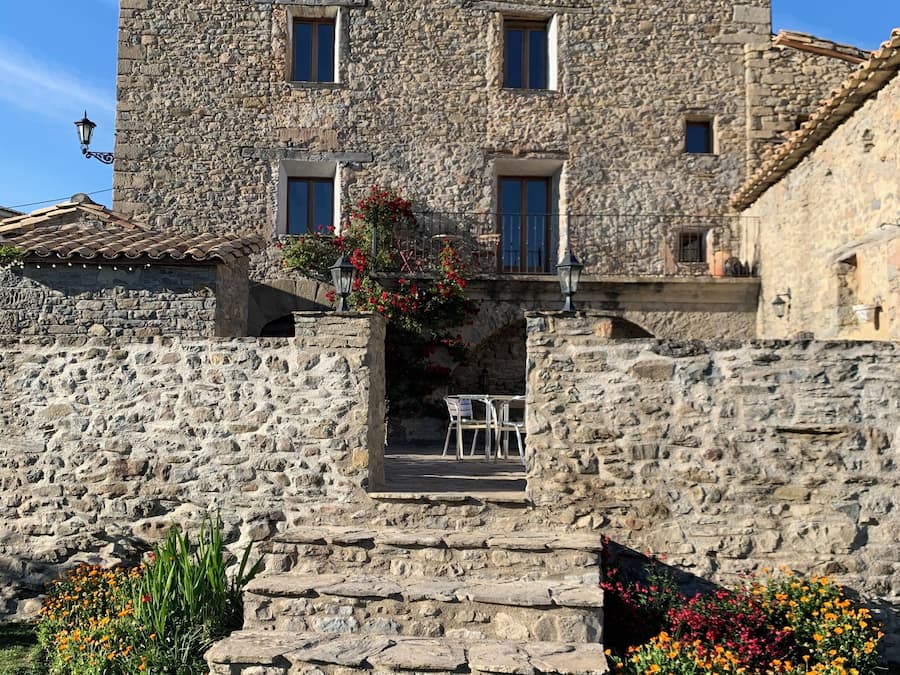 A stone building with a balcony, steps leading up to the entrance, and outdoor seating.