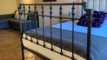 Una cama con estructura metálica, una manta gris y un cojín morado.