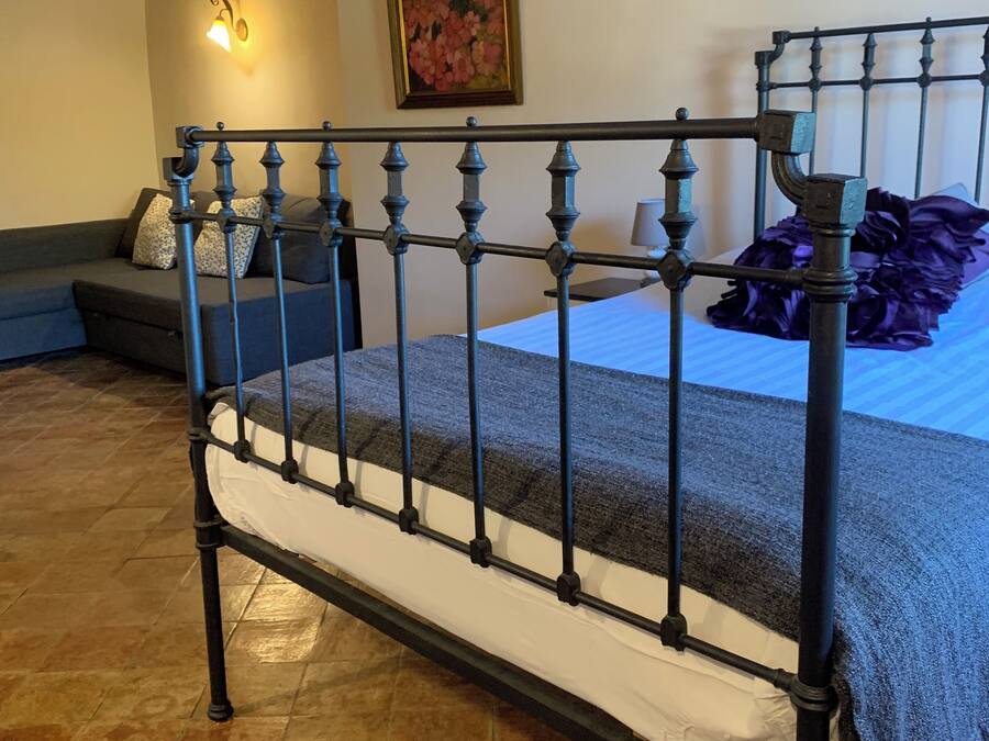 Una cama con estructura metálica, una manta gris y un cojín morado.