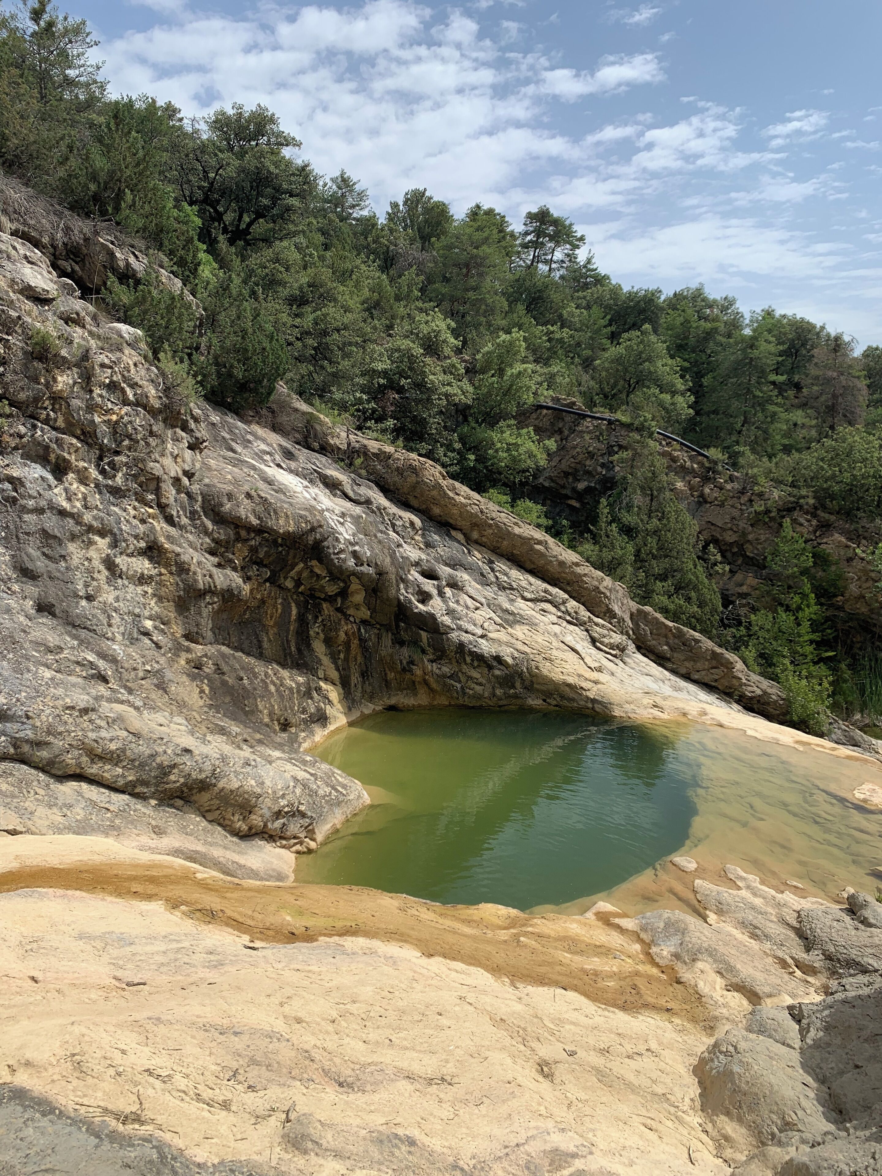 A rocky landscape with a small pond surrounded by trees and a clear sky.