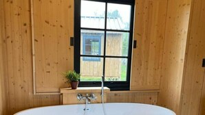 Un baño moderno con una bañera independiente, paneles de madera, un ventanal con vistas y una pequeña planta en maceta.