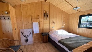 Habitación de cabaña de madera con cama, una silla, una obra de arte con cabeza de ciervo y una ventana.