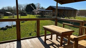 Una terraza de madera con un banco y una mesa, con vistas a una zona vallada que tiene un estanque y un edificio al fondo.
