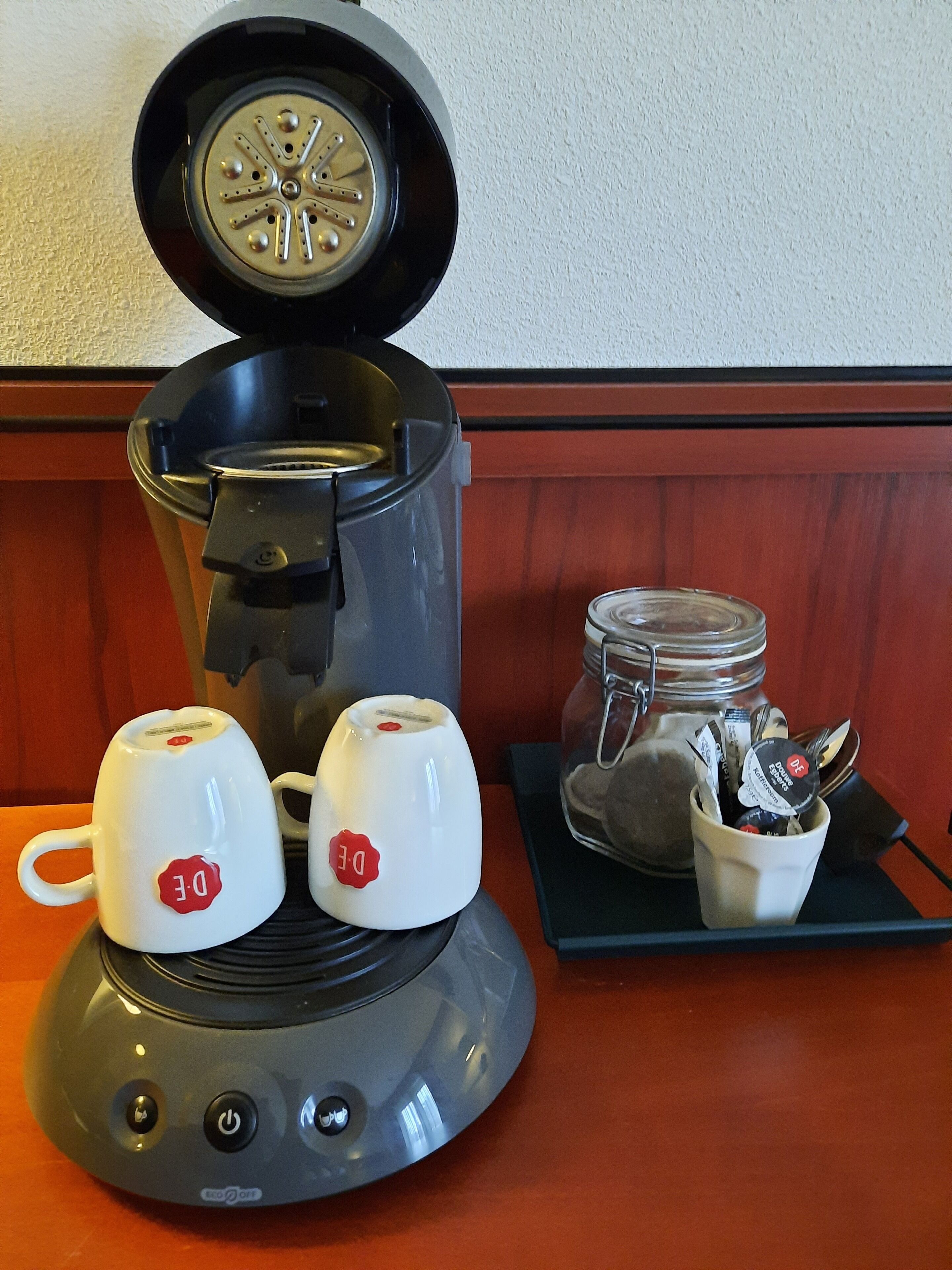 Uma cafeteira com duas chávenas sobre uma mesa, um frasco de açúcar e uma colher.