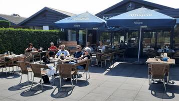 An outdoor cafe with tables and chairs, covered by umbrellas, and a building in the background.
