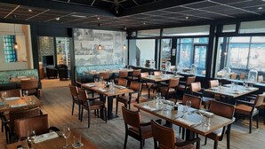 A restaurant with multiple tables and chairs, large windows, and a mural on the wall. - De Schildkamp (Asperen)
