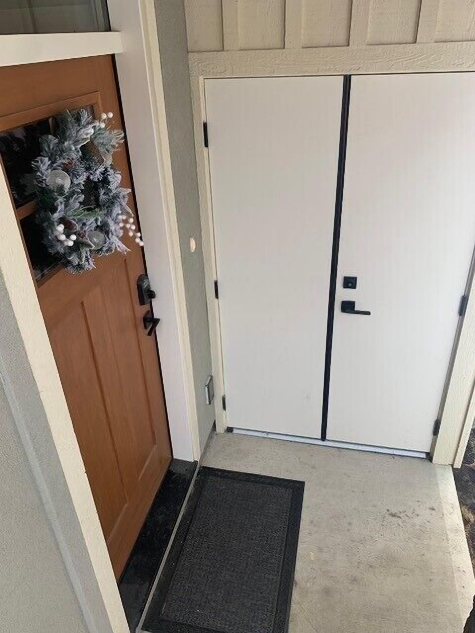A front door with a wooden panel and a white door, a doormat, and a wreath on the left.