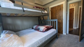 Een slaapkamer met een stapelbed, een houten hoofdbord, een enkel bed met witte beddengoed en een deur naar een andere kamer.