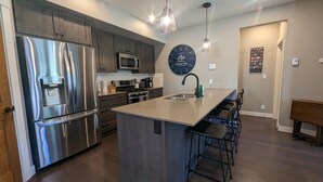 Una cocina moderna con electrodomésticos de acero inoxidable, una isla central con taburetes de bar y un reloj de pared.