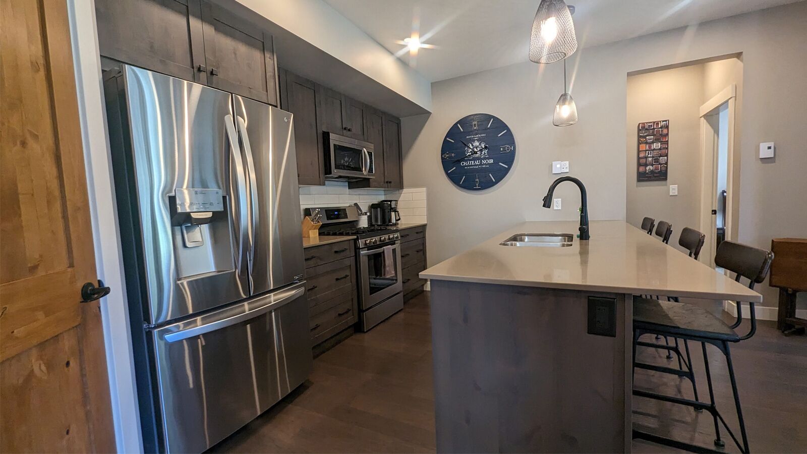 A modern kitchen with stainless steel appliances, a central island with bar stools, and a wall clock.